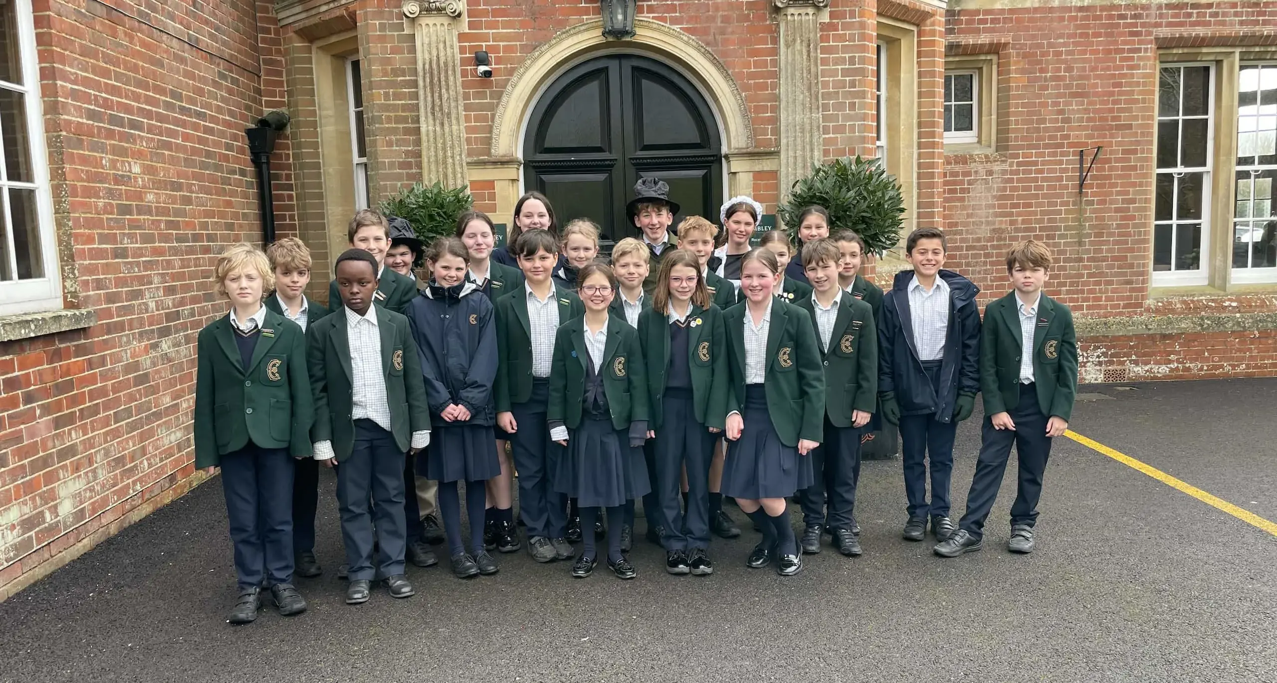 School pupils pose in front of the school smiling at the camera