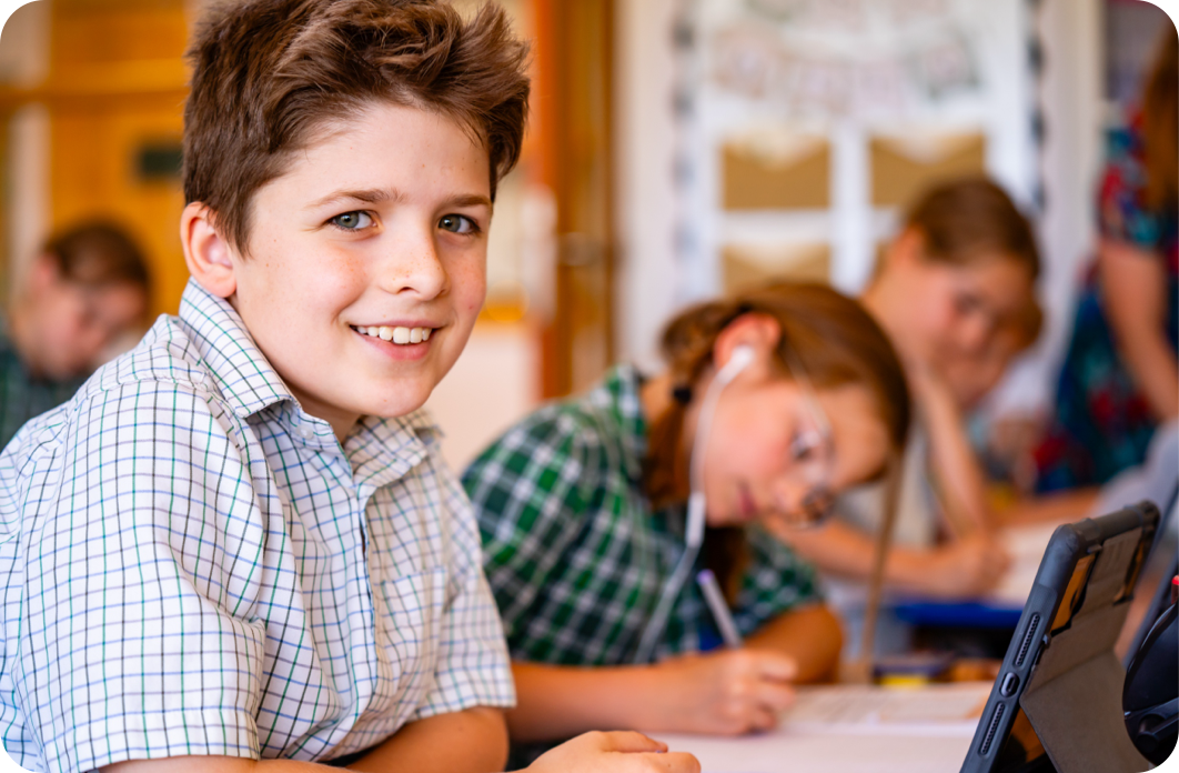 Children in the background doing classwork with a pupil in the foreground smiling at the camera