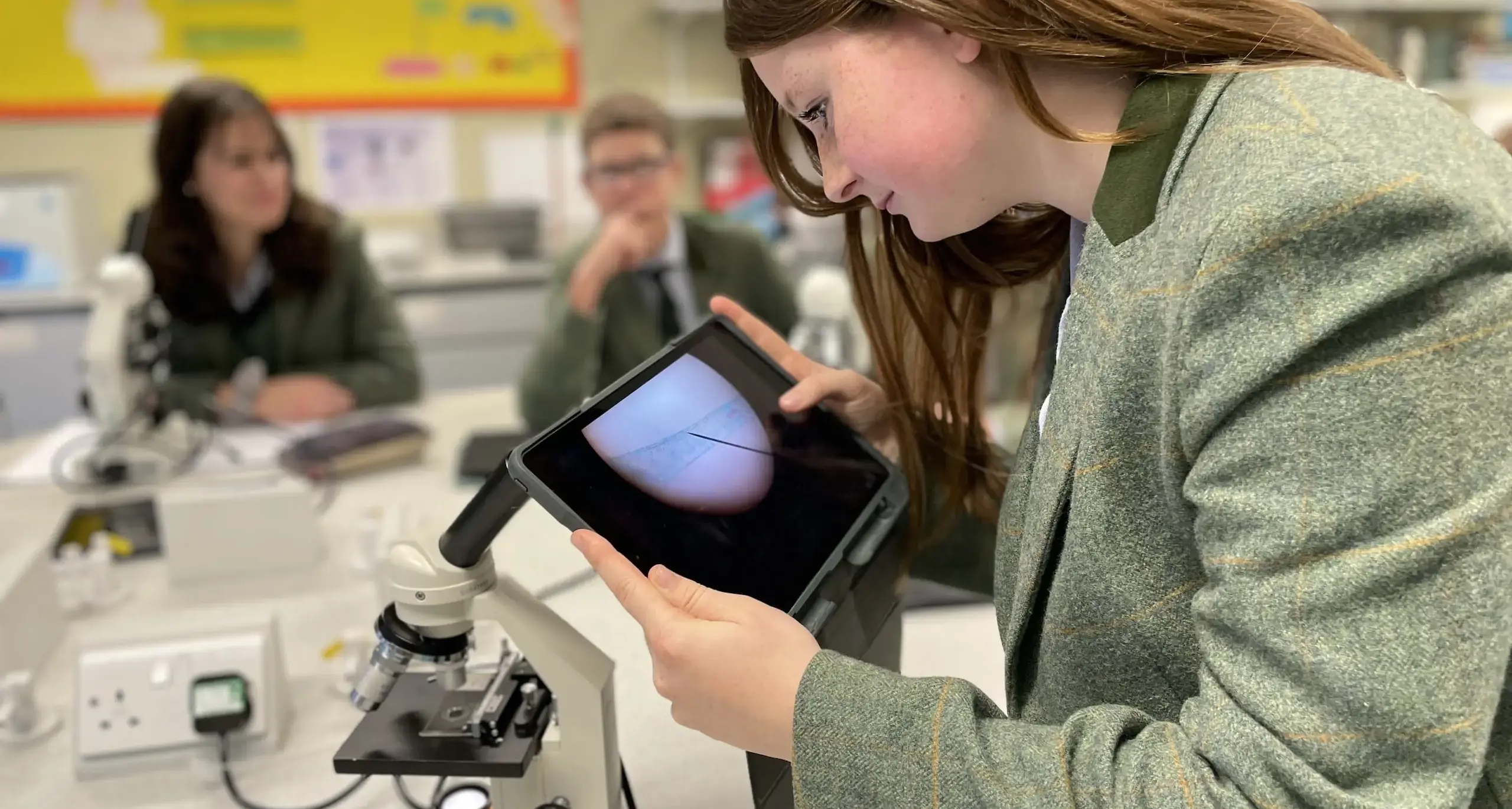 A student uses a digital tablet to view what is being viewed on a microscope