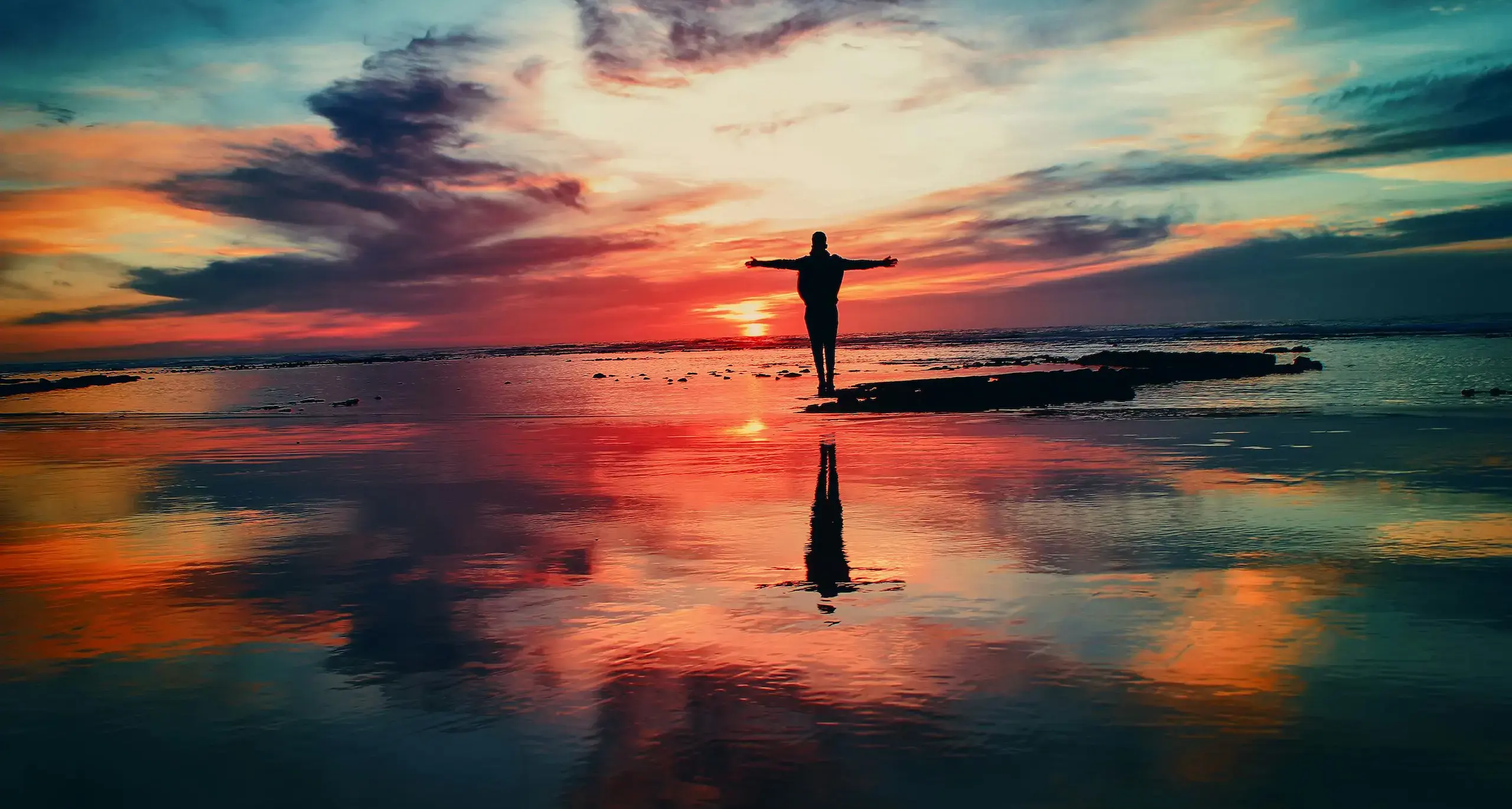 Man standing on a sunset beach with arms outstretched